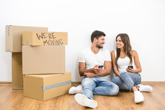 El teléfono de la feliz pareja cerca de las cajas en el fondo de la pared blanca