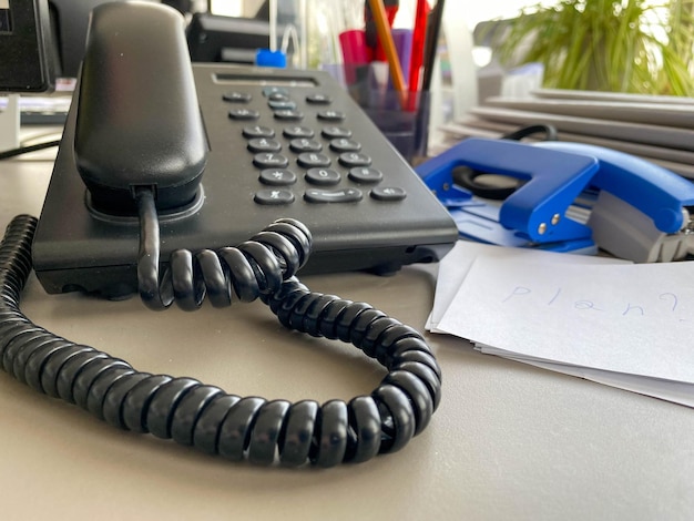 Teléfono fijo negro con botones de tubo y un cable en la mesa de trabajo en el escritorio de la oficina