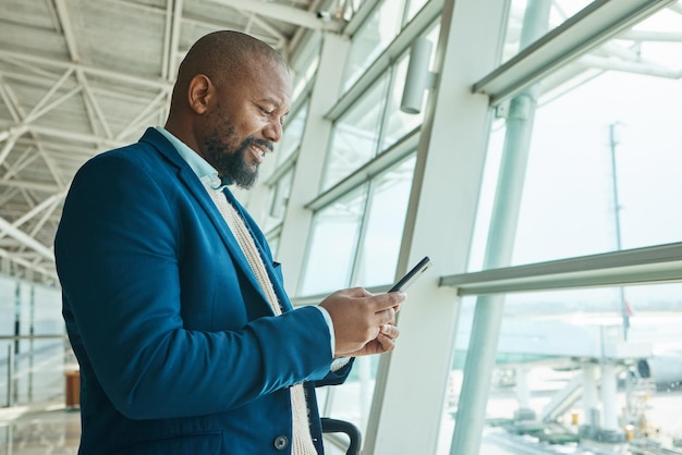 Teléfono de hombre negro y charlando en el aeropuerto para un viaje de negocios o comunicación esperando el vuelo Sonrisa masculina afroamericana para el horario de conversación o revisando los tiempos normales en el teléfono inteligente