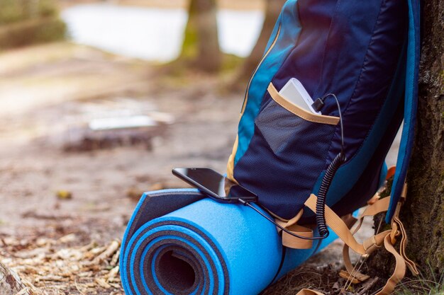 El teléfono inteligente se carga con un cargador portátil. Power Bank carga el teléfono al aire libre con una mochila para el turismo en el fondo de la naturaleza y el río.