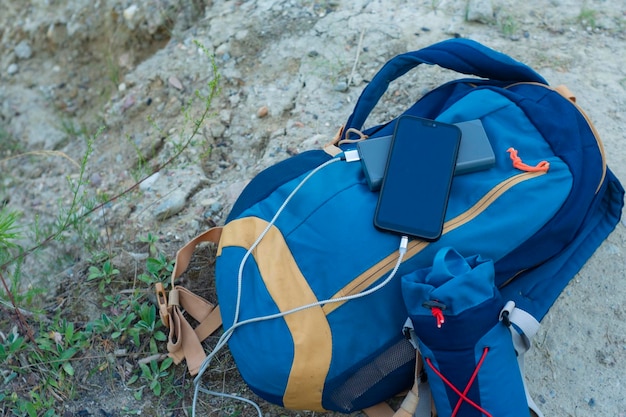 El teléfono inteligente se carga con un cargador portátil Power Bank carga el teléfono al aire libre con una mochila para el turismo en la naturaleza