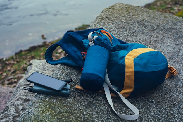 El teléfono inteligente se carga con un cargador portátil. Power Bank carga el teléfono al aire libre con una mochila para turismo en la naturaleza.