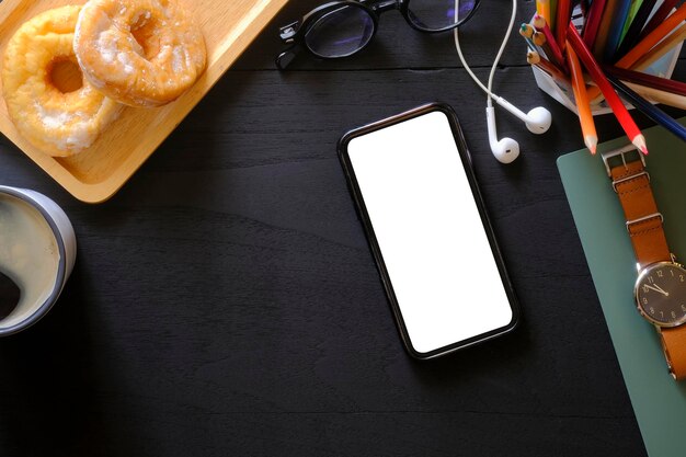 Teléfono inteligente con donuts y suministros de taza de café de pantalla en blanco sobre fondo de madera negra Vista superior