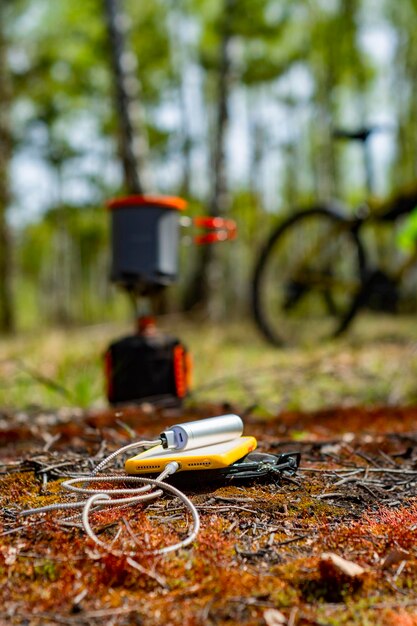 El teléfono inteligente es cargado por un banco de energía en el bosque contra el fondo de un quemador de gas turístico y una bicicleta