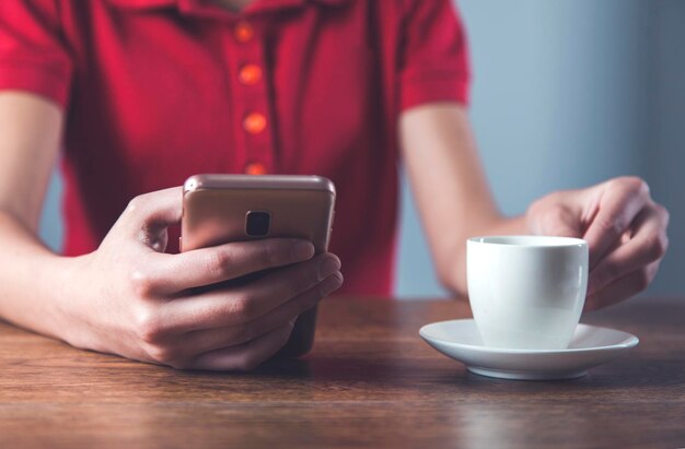 Teléfono inteligente de mano de mujer con taza de café