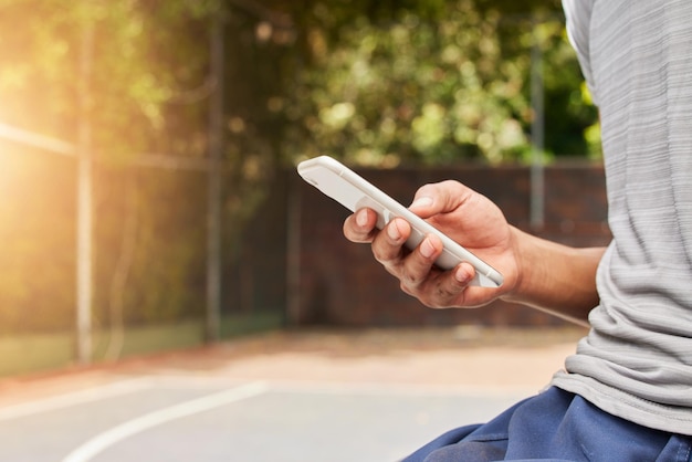 Teléfono inteligente en la mano persona al aire libre y escribiendo desplazamiento en las redes sociales y comunicación con la aplicación móvil Uso del teléfono mientras se envían mensajes de texto en el patio de recreo deportivo y chat en línea con contacto y tecnología