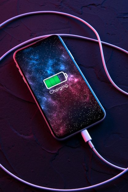 Teléfono inteligente móvil en dispositivo de carga inalámbrica sobre fondo de color rojo y azul neón oscuro. El icono de la batería y el progreso de la carga se iluminan en la pantalla. Smartphones conectados a la fuente de alimentación. Batería baja.