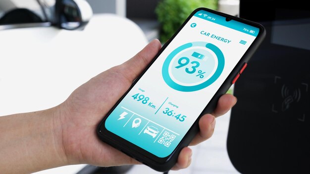 El teléfono inteligente muestra el estado de la batería en una aplicación móvil EV inteligente mientras el vehículo EV recarga electricidad mediante una estación de carga doméstica en el garaje Futuro vehículo EV innovador y sostenibilidad energética Examinar