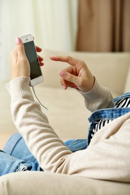 Teléfono inteligente de música en mano femenina en el fondo interior del hogar