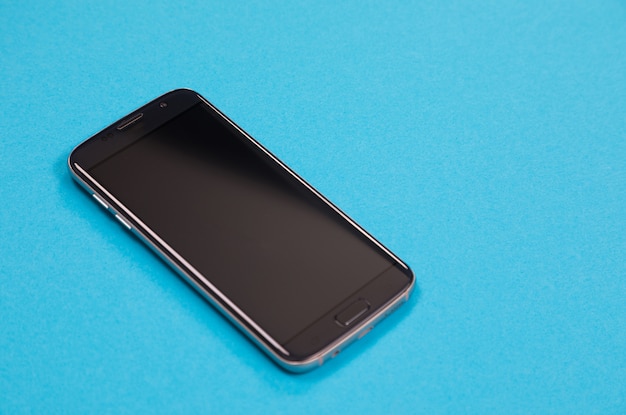 Un teléfono inteligente negro yace sobre la superficie azul aislado