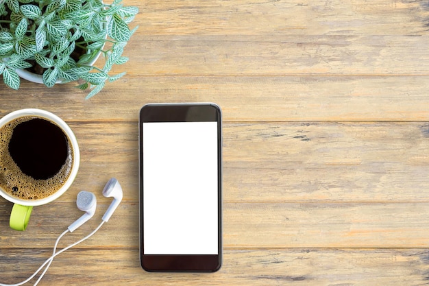 Teléfono inteligente con pantalla blanca, auricular blanco y taza de café en el fondo de la mesa de madera