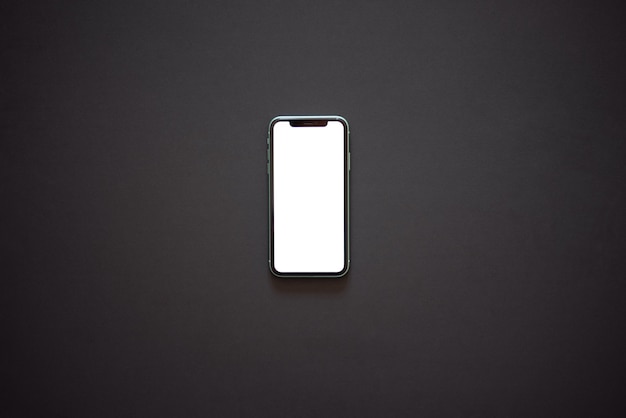 un teléfono inteligente con una pantalla blanca encendida sobre un fondo oscuro vista superior plana