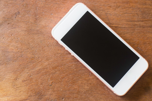 Teléfono inteligente con pantalla en blanco en la mesa de madera