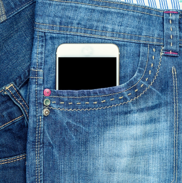 El teléfono inteligente con una pantalla negra en blanco está en el bolsillo delantero de los vaqueros azules
