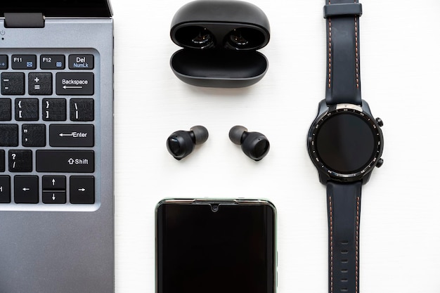 Teléfono inteligente portátil Auriculares inalámbricos y reloj sobre fondo blanco Gadgets modernos Vista superior
