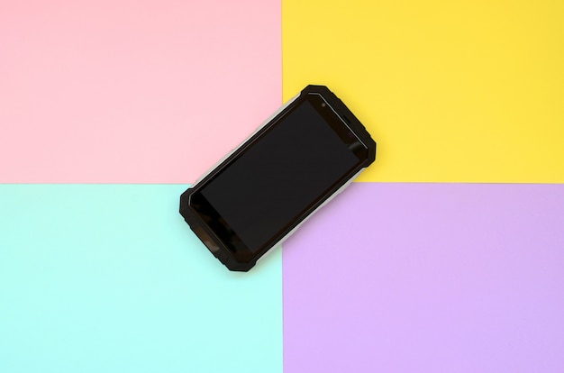 Un teléfono inteligente a prueba de golpes negro se encuentra en un fondo de color pastel