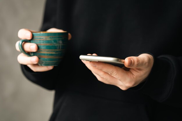 El teléfono inteligente y la taza de café hecha a mano en manos de un hombre cierran el concepto de usar tecnología