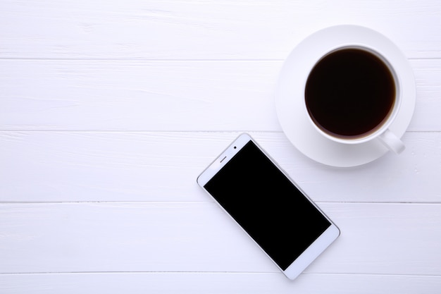 Teléfono inteligente con taza de café en madera blanca