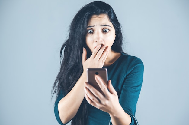 Teléfono de mano mujer sorprendida sobre fondo gris