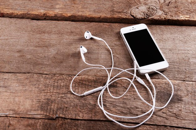 Teléfono móvil blanco con auriculares sobre fondo de madera