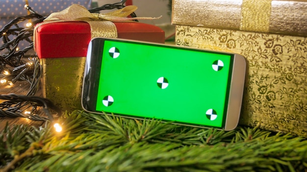 Teléfono móvil con Chroma key verde en pantalla sobre adornos navideños y regalos