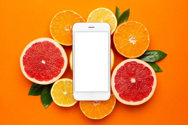 Teléfono móvil y cítricos sobre un fondo naranja