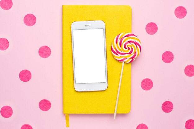 Teléfono móvil con un cuaderno amarillo y una paleta de colores en rosa con confeti