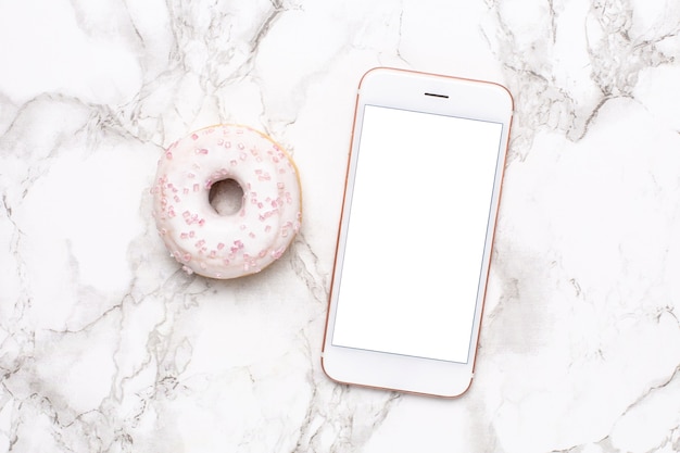 Teléfono móvil y donut dulce sobre un fondo de mármol