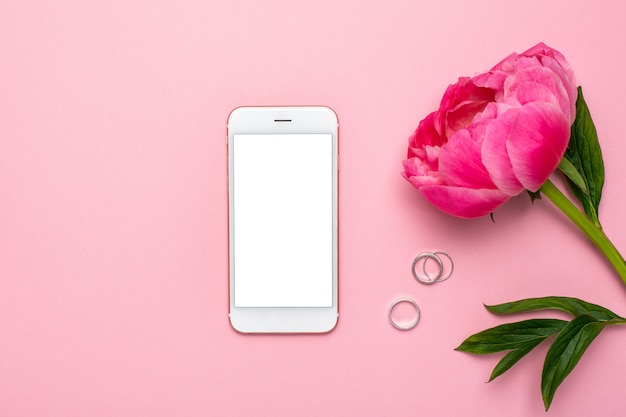 Foto teléfono móvil y flor de peonía en mesa de color rosa pastel en estilo plano laico.