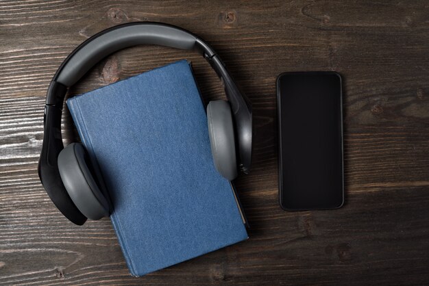 Teléfono móvil y libro con auriculares sobre fondo de madera. Concepto de audiolibro. Vista superior, copia espacio.