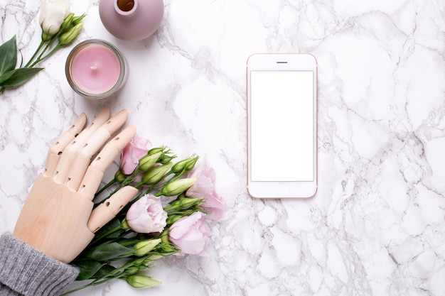 Teléfono móvil y mano de madera con flores rosas sobre mármol