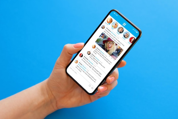 Teléfono móvil en mano sobre fondo azul con aplicación de microblogging de redes sociales de muestra en la pantalla