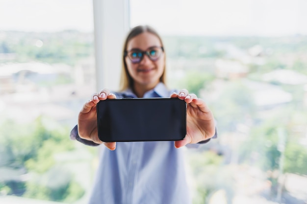 Un teléfono móvil moderno con una pantalla negra se sostiene en manos de una mujer con un teléfono inteligente cerrado