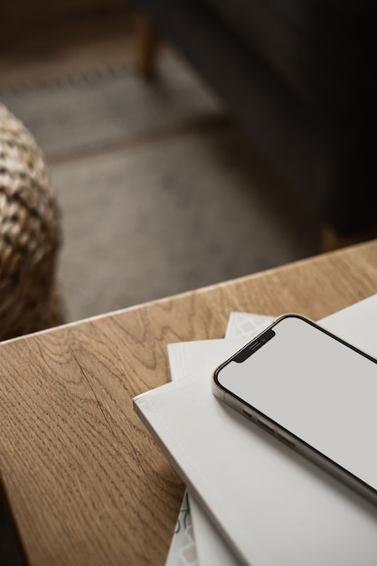 Teléfono móvil de pantalla en blanco, hojas de papel sobre mesa de madera y alfombra