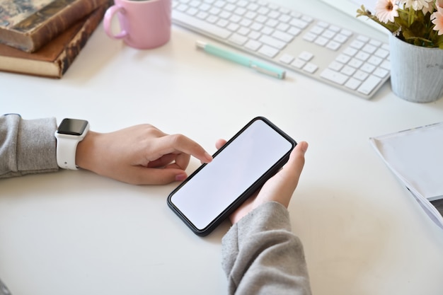 Teléfono móvil con pantalla en blanco en mano femenina en trabajo de escritorio en oficina en casa