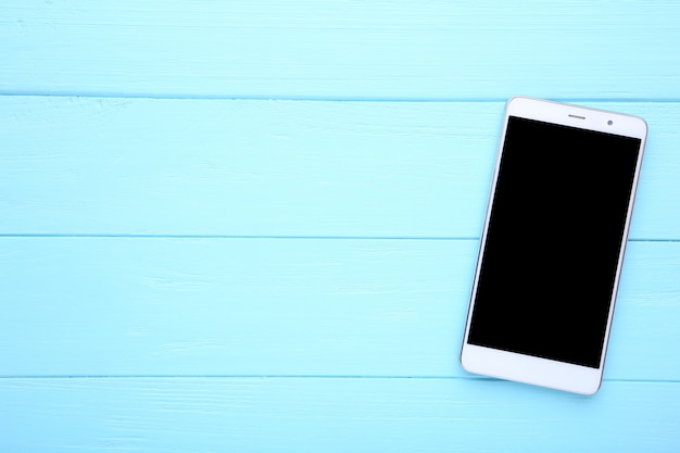 Teléfono móvil con pantalla en blanco sobre fondo de madera azul. Smartphone en mesa de madera.