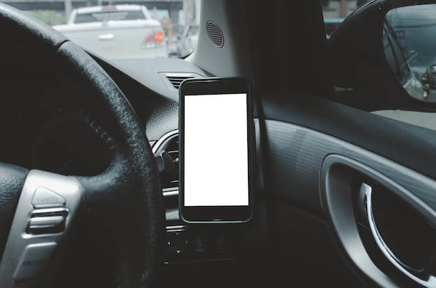 Teléfono móvil en la rejilla de ventilación del coche. En blanco con pantalla blanca. Simulacros de teléfono inteligente en el coche.