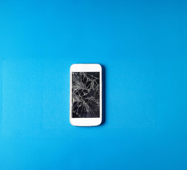 Teléfono móvil roto con pantalla rota sobre fondo de papel de color azul
