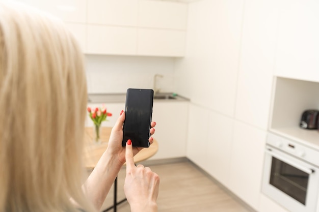 Teléfono móvil con sistema de control del hogar en una pantalla. Casa inteligente, domótica, dispositivo con iconos de aplicaciones. La mujer usa su teléfono inteligente con la aplicación de seguridad smarthome para abrir la puerta de su casa.