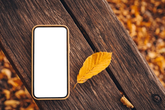 Teléfono móvil sobre fondo de madera y hojas de otoño