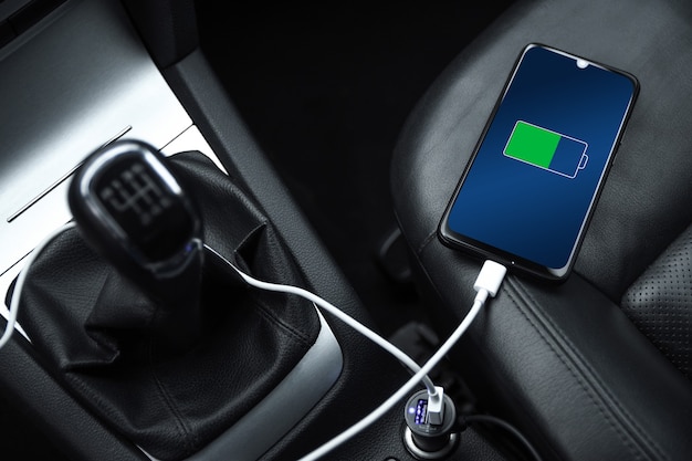 El teléfono móvil, teléfono inteligente, teléfono celular está cargado, cargue la batería con el cargador USB en el interior del automóvil. Interior del coche negro moderno.