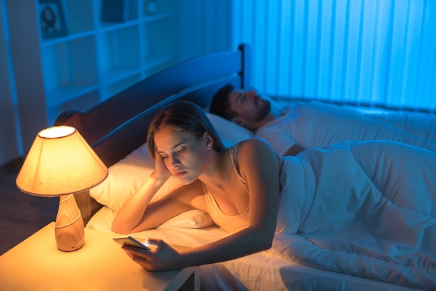 El teléfono de la mujer atractiva en la cama. Noche