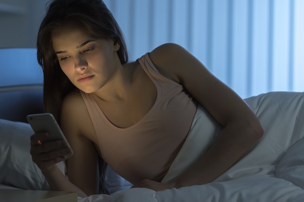 El teléfono de la mujer atractiva en el dormitorio. Noche