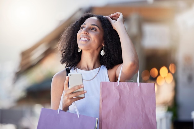 Teléfono de mujer negra y bolsa de compras minorista de un cliente en una aplicación de tienda en línea para descuento Promoción de tiendas redes móviles urbanas y de comercio electrónico de una mujer en una calle de la ciudad con fondo borroso