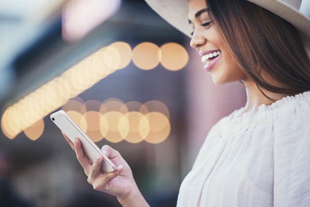 Teléfono de mujer y sonrisa para las redes sociales en la ciudad para viajes de comunicación o conversación Mujer feliz sonriendo para discutir viajes o conexión 5G en línea en un teléfono inteligente en una ciudad urbana