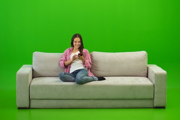 El teléfono de la mujer de la sonrisa en el sofá en el fondo verde