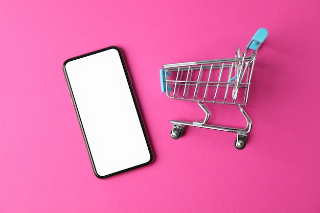 Foto teléfono con pantalla vacía y carrito de compras sobre fondo rosa, vista superior