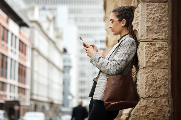 Teléfono de la pared de la ciudad y mujer de negocios escribiendo investigación en línea leyendo correo electrónico y desplazándose en la aplicación del sitio web o en las redes sociales El teléfono celular de la acera urbana y la persona profesional se relajan en el descanso de trabajo al aire libre