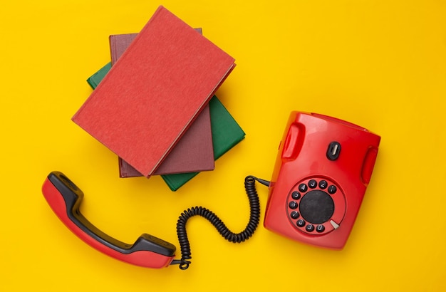 Foto teléfono rotativo antiguo rojo retro y libros sobre fondo amarillo vista superior