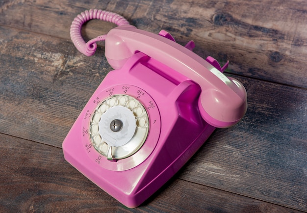 Teléfono rotatorio rosado retro en la mesa de madera